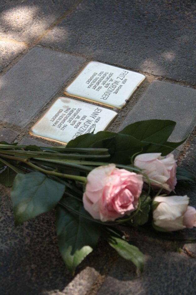 Detailaufnahme von zwei Stolpersteinen und daneben abgelegten rosafarbene Rosen